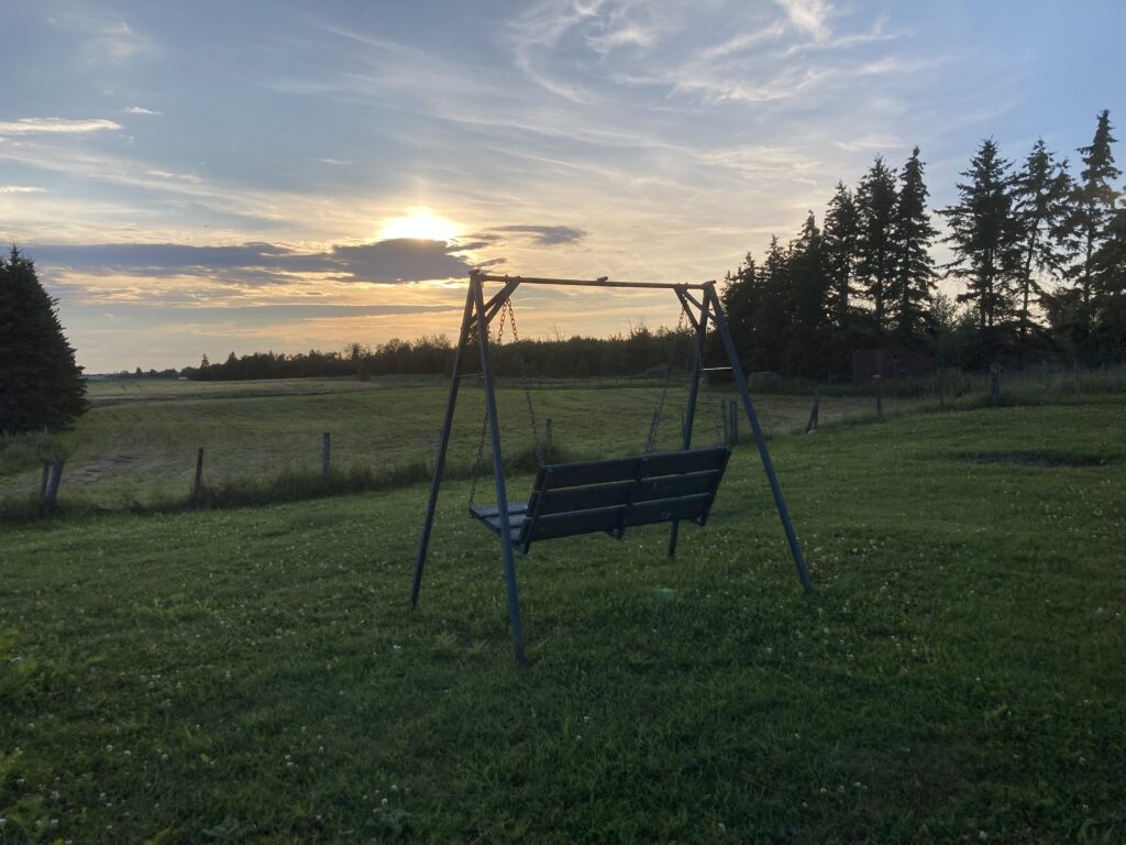 A two-seater swing sits facing the setting sun.